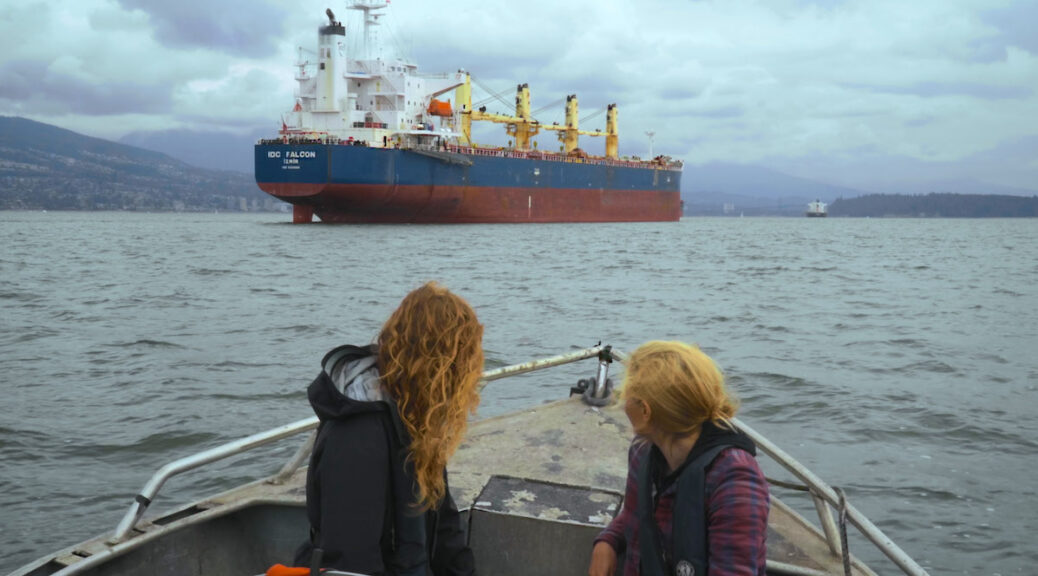 Two women in a boat looking at a nearby oil tanker