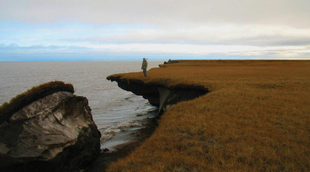 man standing near the edge of a cliff, part of which has dropped into the ocean