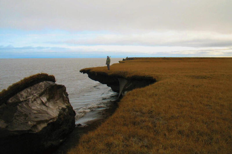 man standing near the edge of a cliff, part of which has dropped into the ocean