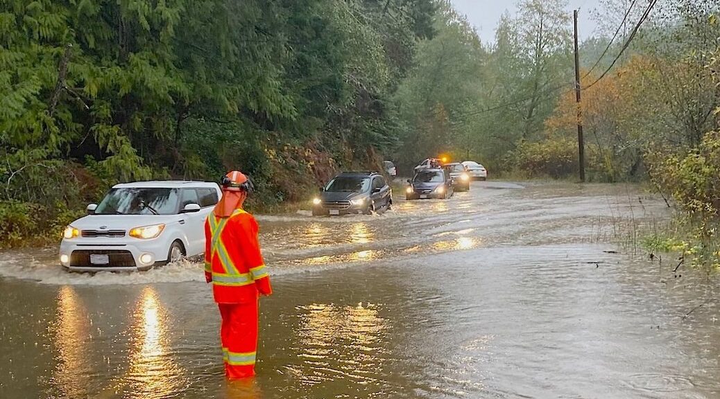 worker in raingear watching cars pass through flooded road