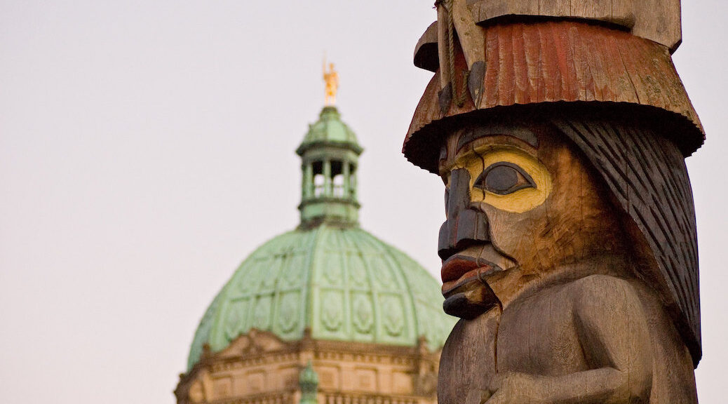 The dome of the BC legislature seen behind a totem pole