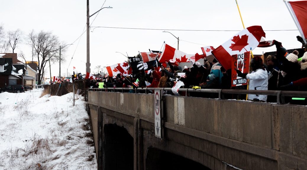 crowd of people bearing Canadian flags and freedom signs on an overpass