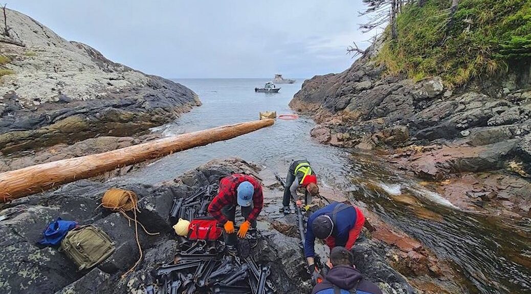 3 men working on a cable emerging on a rocky shore