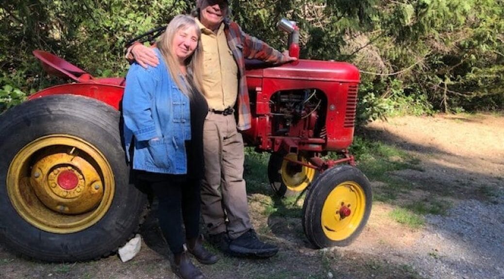 An elderly man and woman beside an antique red tractor red
