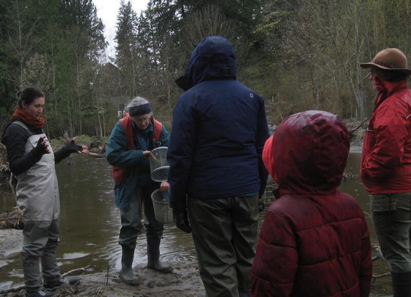 While an older woman sets the fish trap besde the pond, a younger one adresses a small crowd