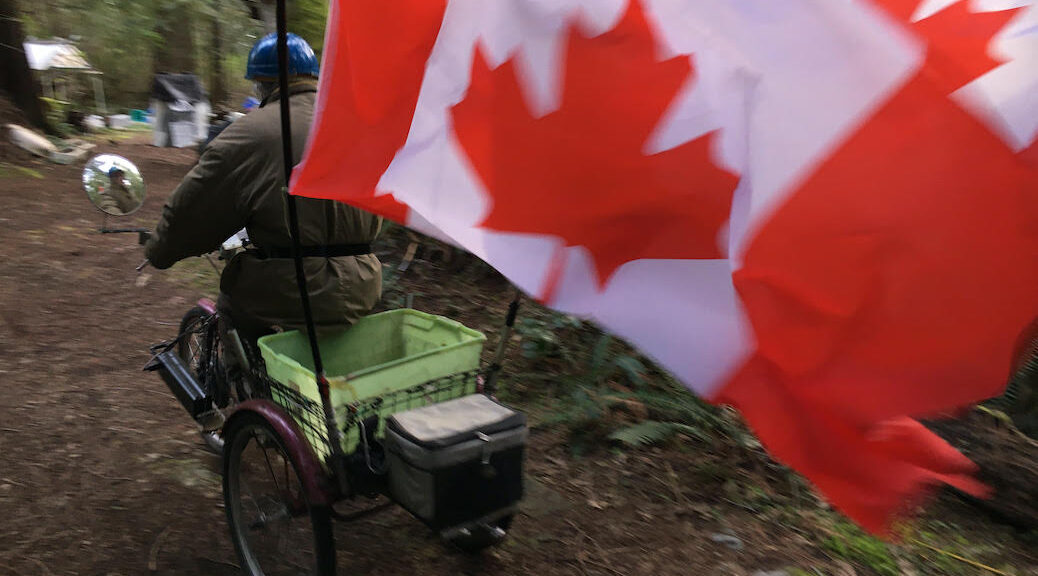 man on electric tricycle, with Canadian flag behind