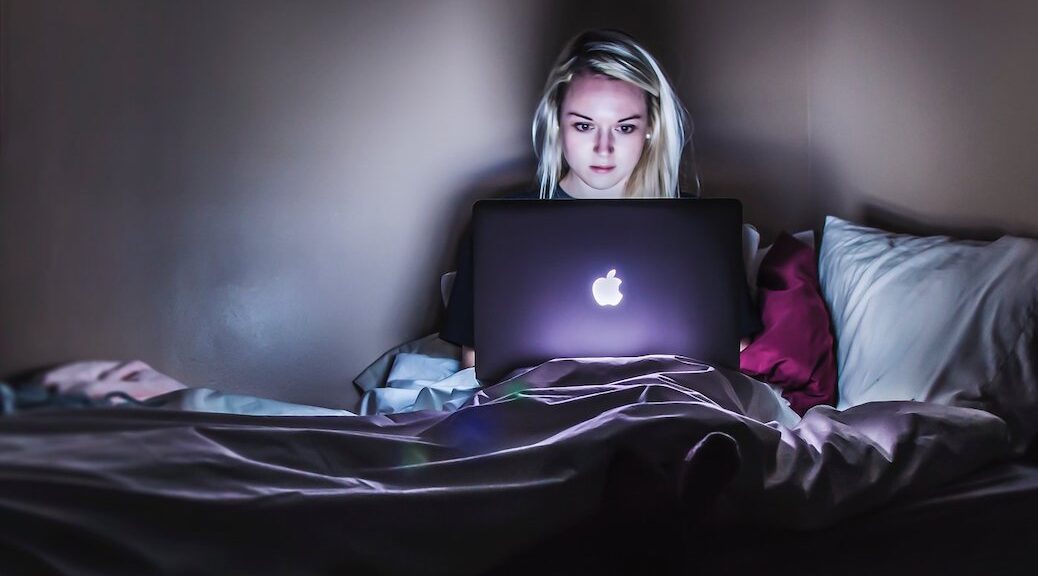 Woman sitting on bed with open MAc computer in her lap