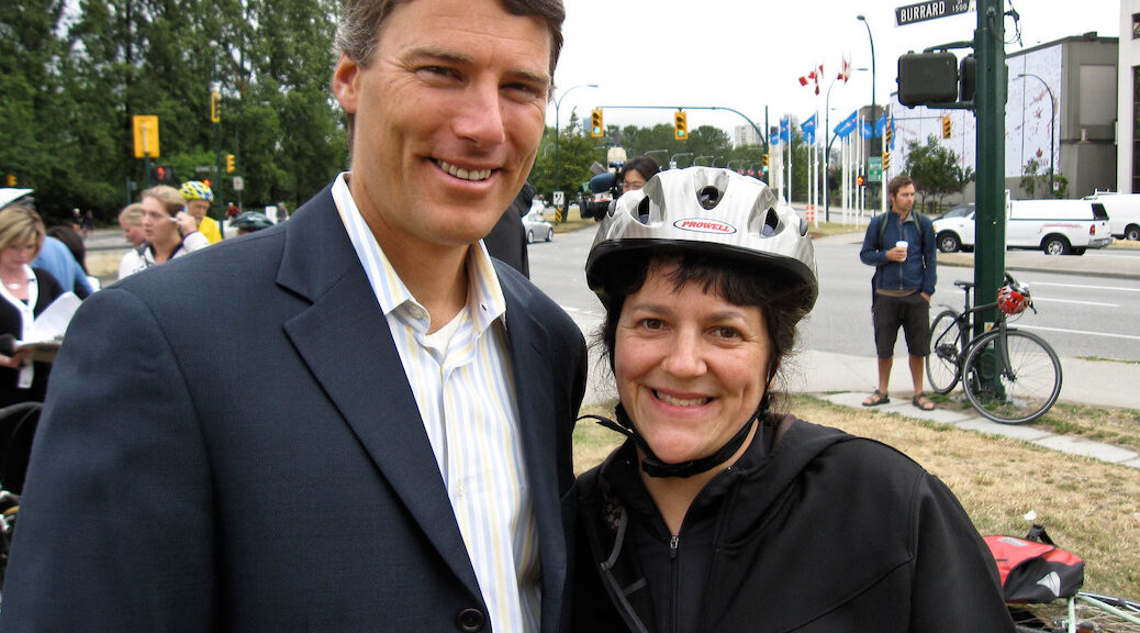 A handsome man standing beside a woman wearing a cycling helmet on a city street