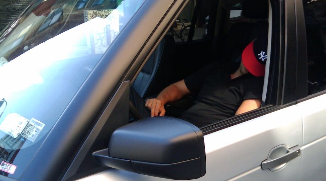 Man with baseball cap pulled over his eyes sleeping in the front seat of a car