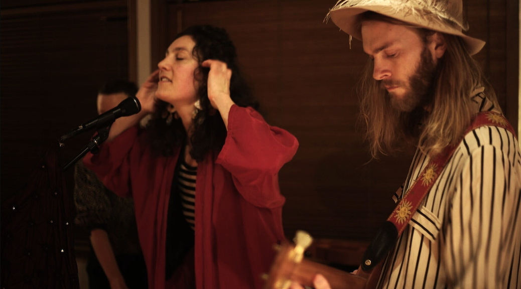 A woman singing into a mic, while a man plays on a guitar