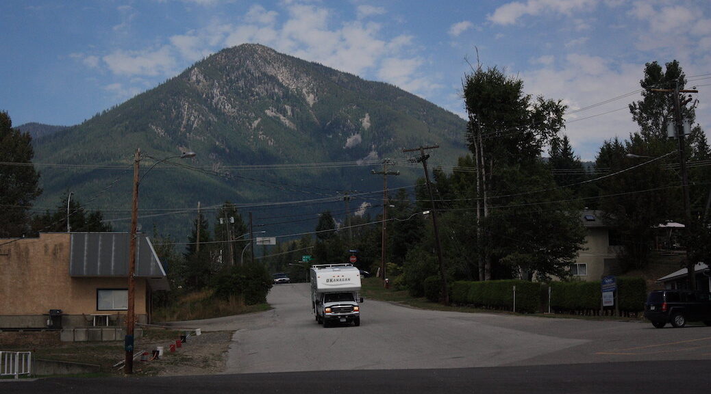 A camper truck drives along a rural community road, there is a mountain in the background