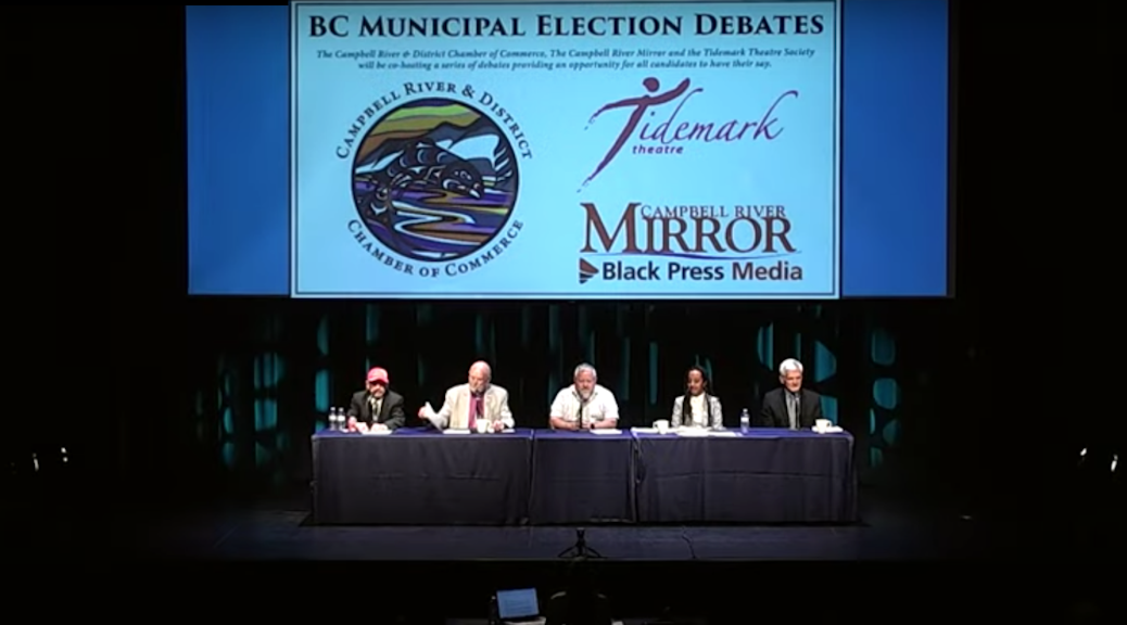 five people sitting on a stage. The words BC Municipal Elections Debates apper on the screen behind them