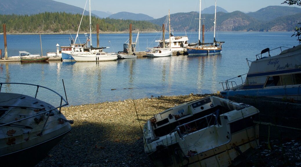 looking from three abandoned vessels on the beach towards a number of boats tied up along a whafr