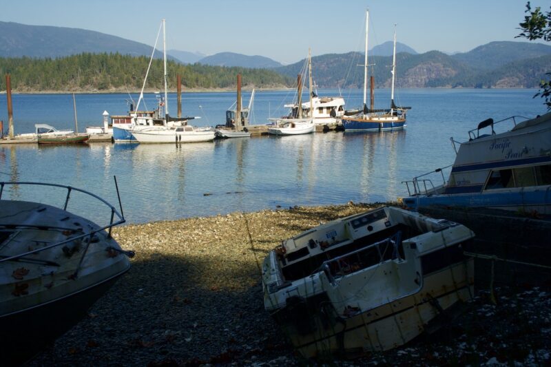looking from three abandoned vessels on the beach towards a number of boats tied up along a whafr