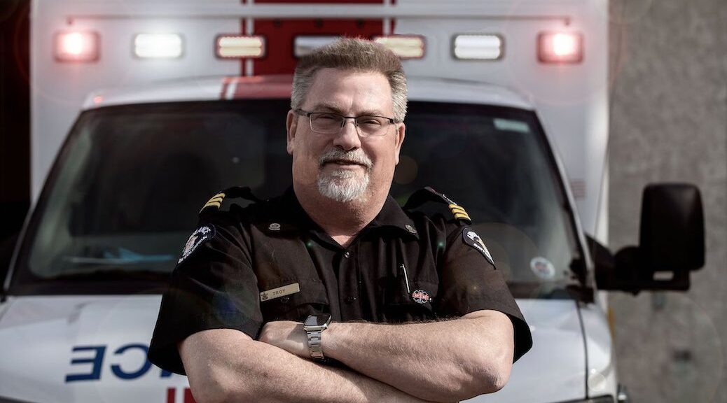 Bearded man in a paramedics uniform standing in front of an ambulance