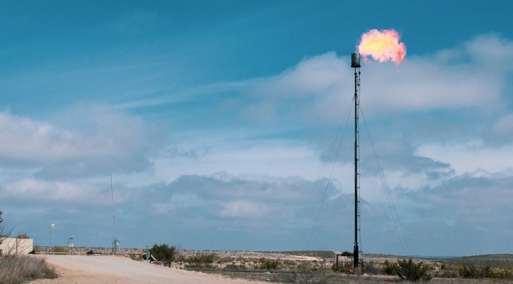 Flames shooting out of a tall stack at a natural gas facility in the desert