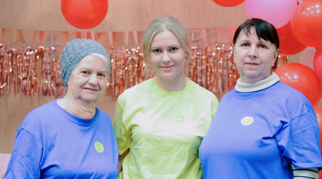Three women, from three generations, two of them in what looks like hospital gear, look at the camera