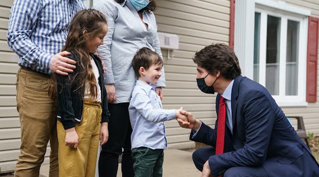 Man in a suit kneels to shake the hands of a young boy, while the boy's parents and sister look on.
