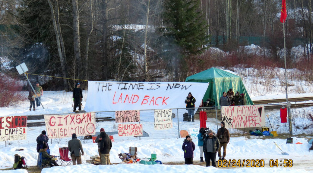 A group of Indigenous people with signs saying things like 'The Time is now, Land Back'