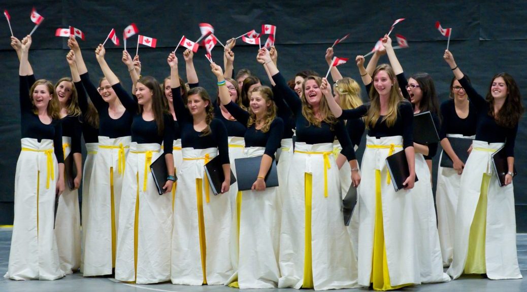 A group of young women, dressed in white skirts and black tops, waving Canadian flags