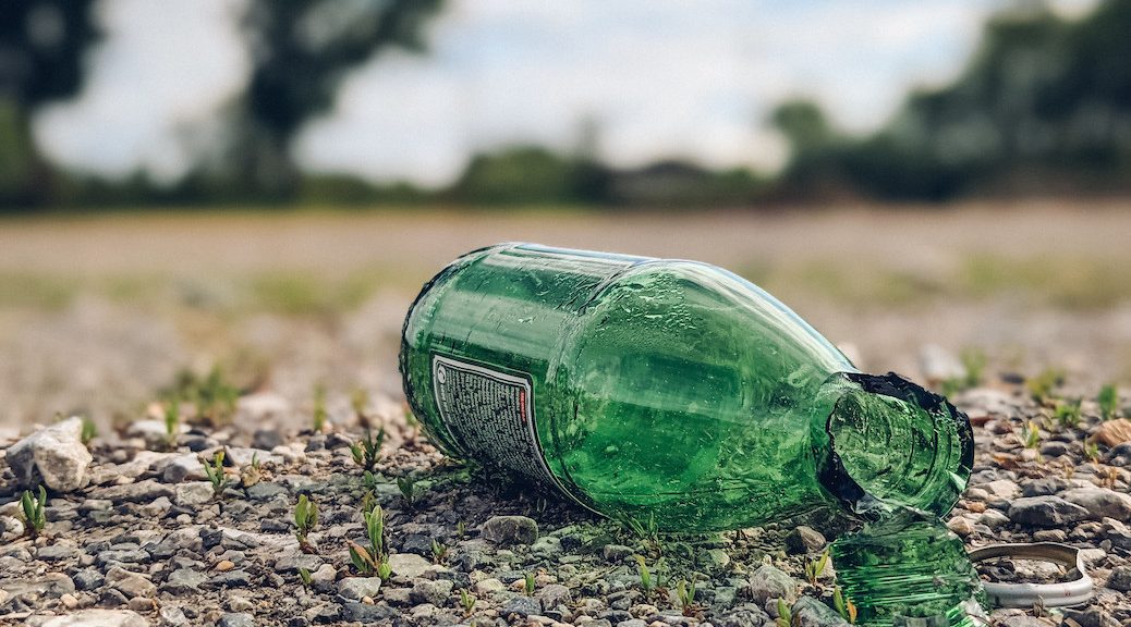 A broken green glass bottle lying in gravel.