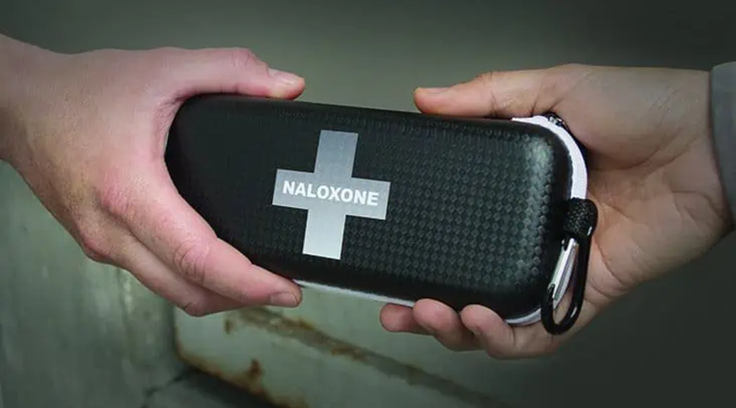 Two hands hold a small black container, with the word 'Naloxone' appearing in a silver cross