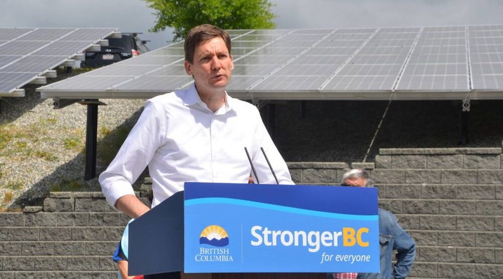 Man speaking from podium, beside array of solar panels