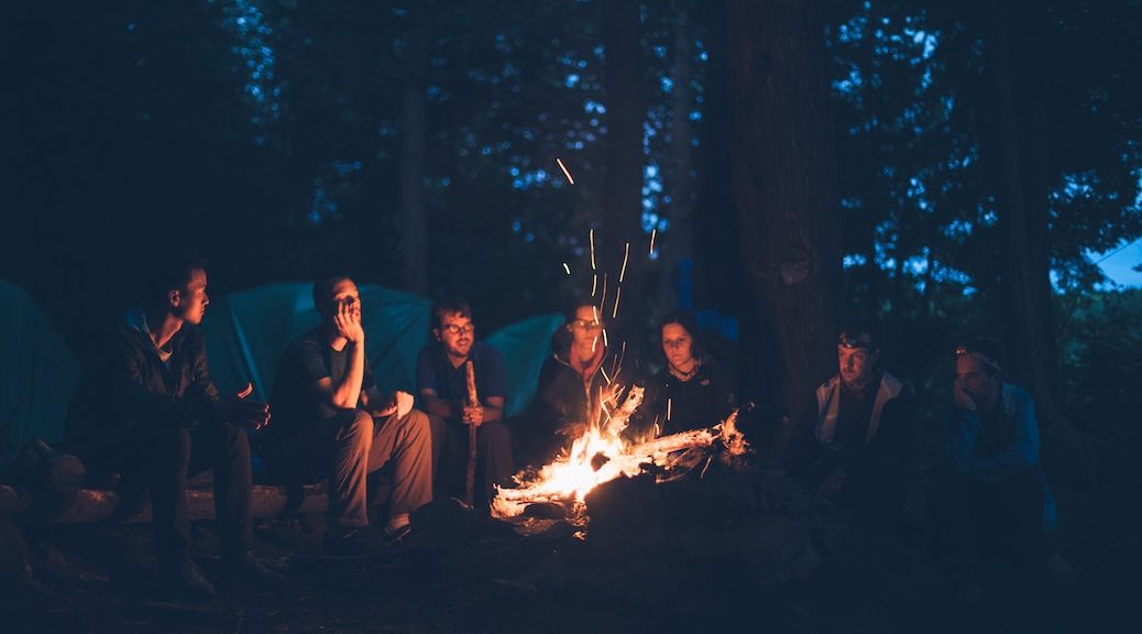 Half a dozen people gathered around a campfire.