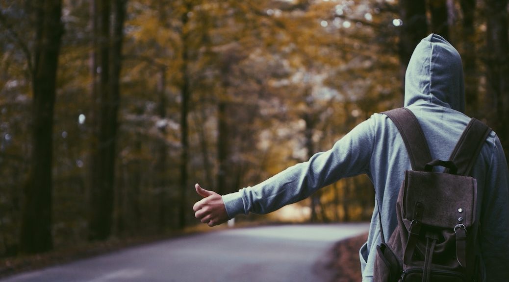 Man wearing hoodie hitchhiking on a country road