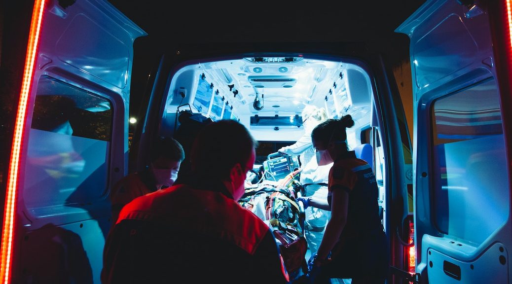 View from the interior of an ambulance. The staff are wearing masks. A patient is being unlaoded into an emergency room area