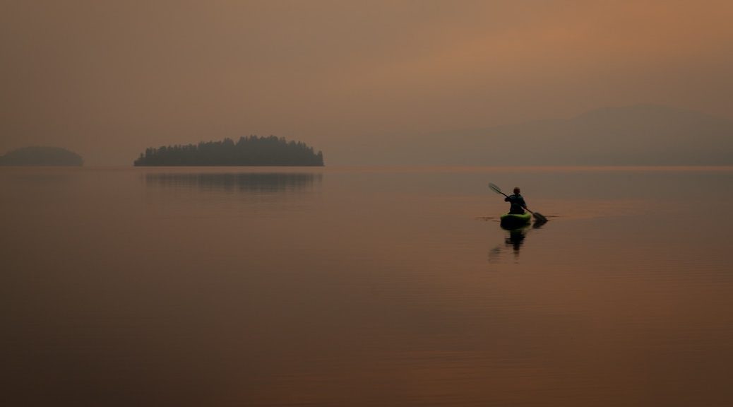 Someone paddling a kayak into a smoke filled lake