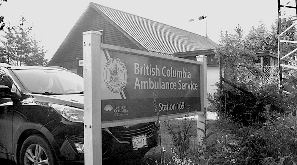 A sign saying British Columbia Ambulance Service stands in front of a parked truck.