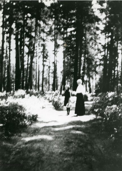 A young girl and elderly woman walking on a dirt road through the forest
