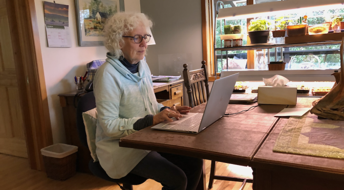 A woman sitting at what appears to be a kitchen table, typing on her laptop