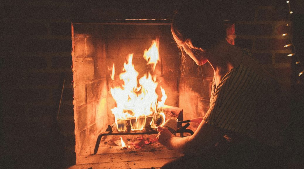Woman in dark room squatting to poke fire in fireplace