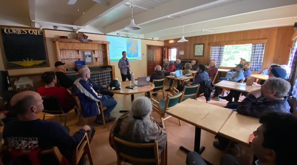 woman in front of screen displaying water cycle image, speaking to roomfull of people