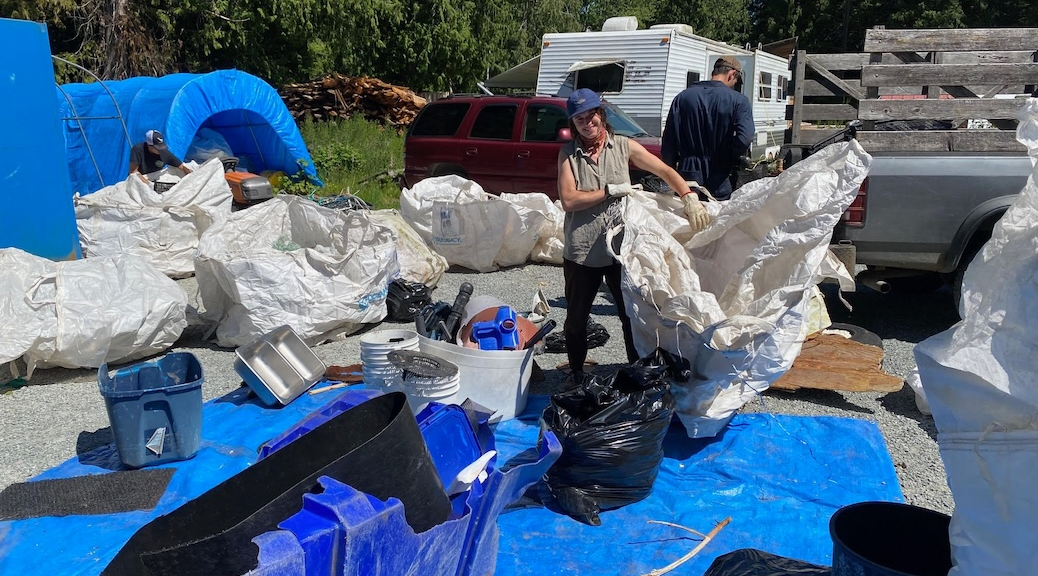 woman sorting beach clean-up debris on a blue tarp. There is a bin behind her