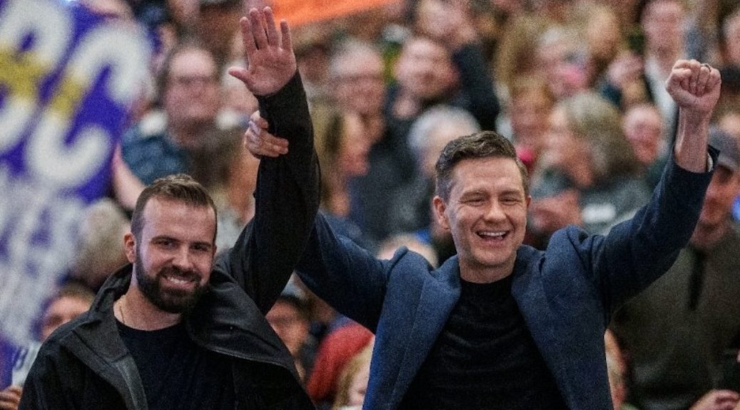 Pierre Poikievre raising Aaron Gunn's arm amidst a bunch of cheering people