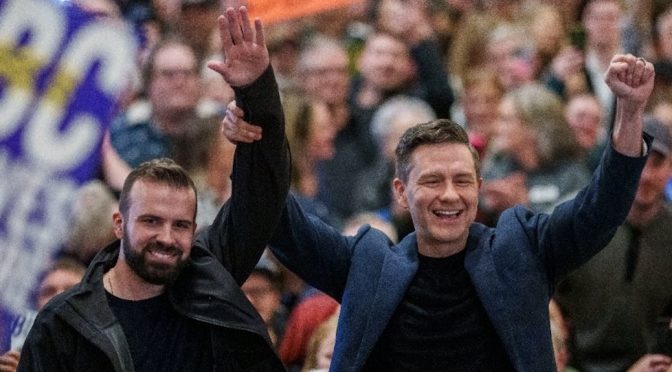 Pierre Poikievre raising Aaron Gunn's arm amidst a bunch of cheering people