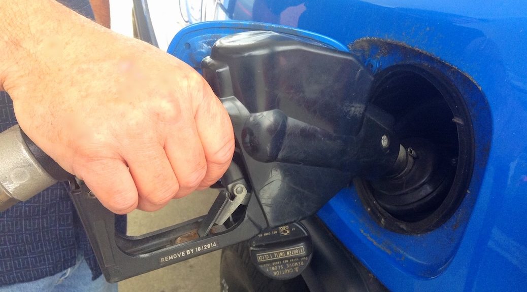 A hand squeezing the trigger of a gas pump nozzle. It is inserted into a car.