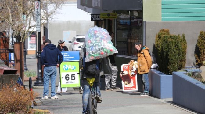 cyclist with large polastic bag on his shoulders, procceds down a crowded street