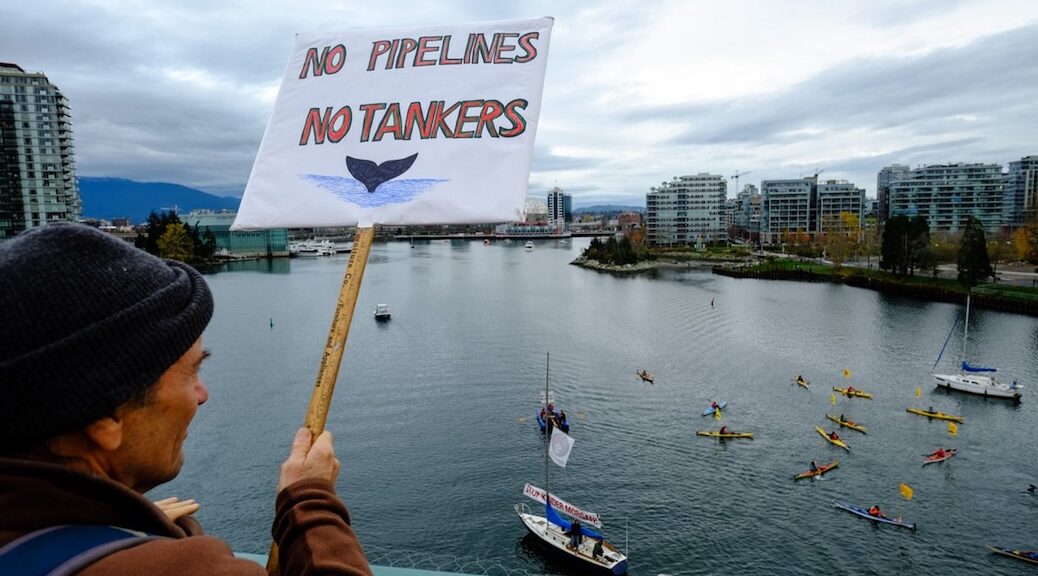 Man overlooking harbour holds up sign saying "No Pipelines No Tankers"