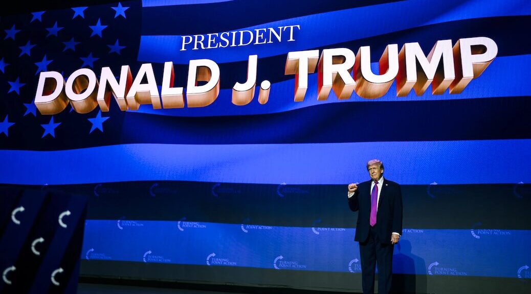 Donald Trump beneath a giant display saying President Donald J Trump