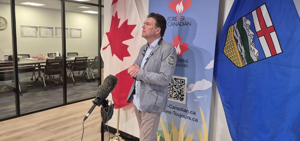 Man standing behind a mic, Canadian maple Leafs are displayed behind him