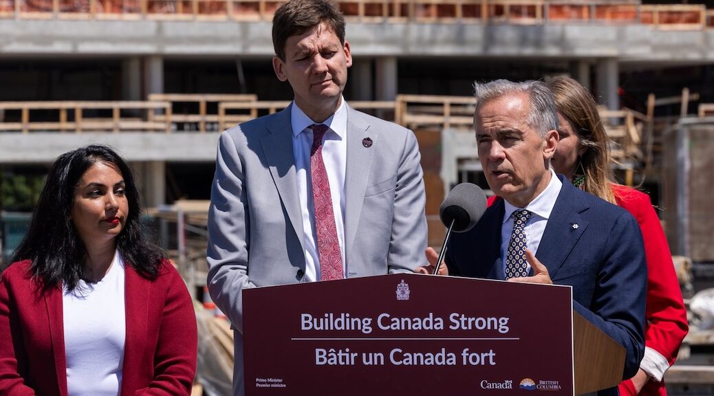 Premier David Eby and Prime Minister Mark Carney stand in front of an unfinished apartment building