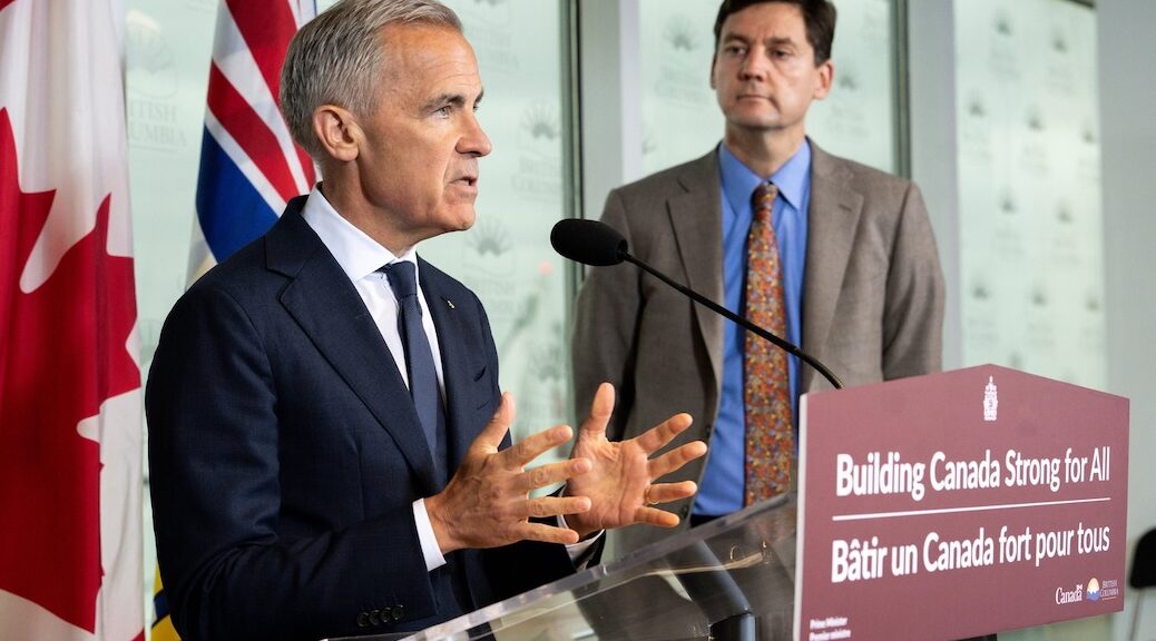 Prime Minister Mark Carney at a podium announcing new pipleine deal. Premiere David Eby looks on.