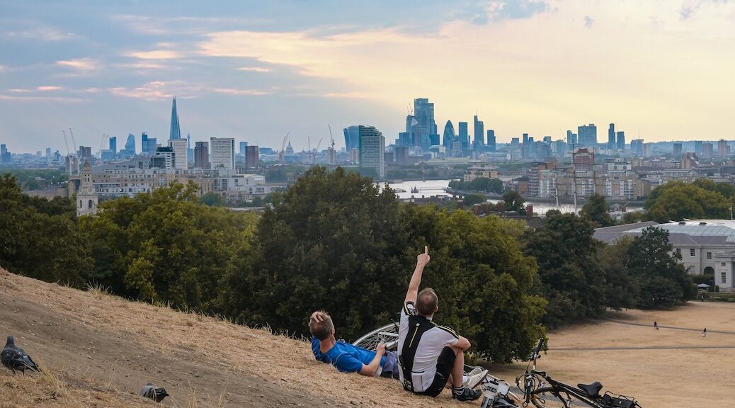 Two cyclists resting in grass that a drought has turned to straw, looking towards LOndon
