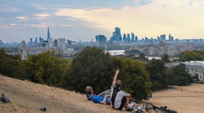 Two cyclists resting in grass that a drought has turned to straw, looking towards LOndon