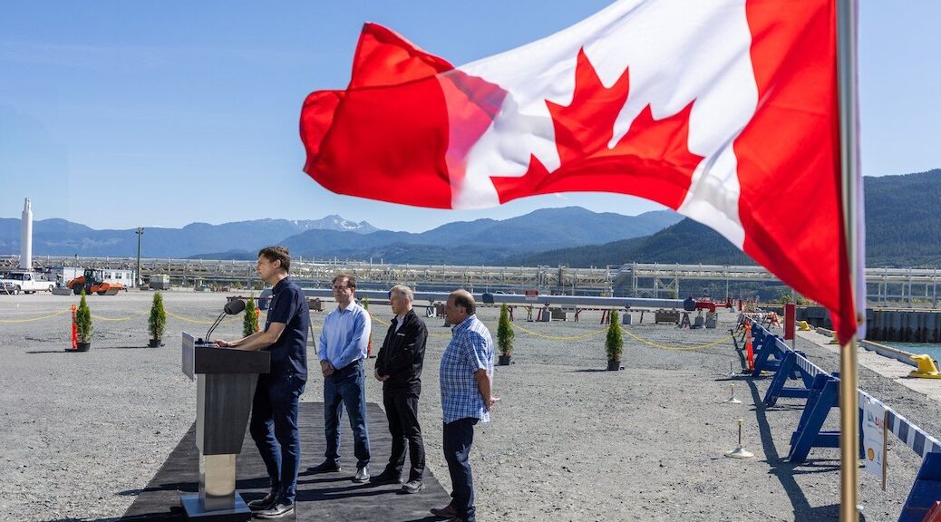 The Canadian flag is fapping in the wind. Premier David Eby speaks during a July 29, 2025 tour of LNG Canada in Kitimat, BC, with Energy Minister Adrian Dix.